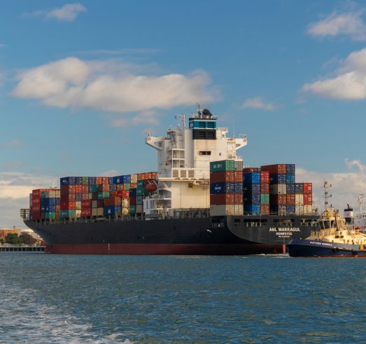 Foto över ett stort fartyg lastat med många containers i en hamn.